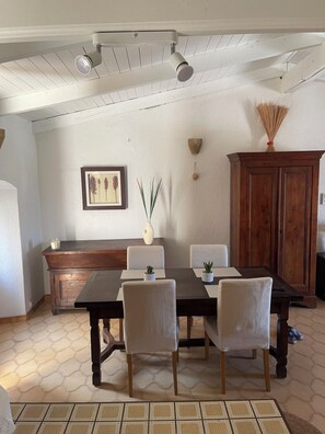 A dining area with a wooden table, white chairs, a cabinet, and a ceiling fan. - Large Studio Apartment in Lunghignano (Montegrosso)