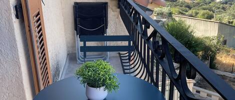 A balcony with a round table and a potted plant, overlooking a mountainous landscape.