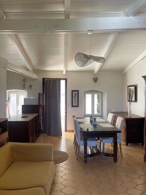 A spacious living area with a dining table, sofa, and kitchen area with cabinets and a refrigerator. - Large Studio Apartment in Lunghignano (Montegrosso)