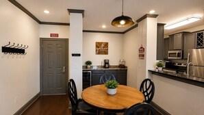 A compact kitchen with modern appliances, a dining area with a wooden table and chairs, and a hanging light fixture. - Welcome to Tusk & Tide! (Tuscaloosa)