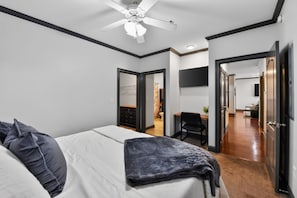 A bedroom with a bed, a desk, and a chair. There is a ceiling fan and a TV mounted on the wall. - Tusk & Tide | Near the Stadium & Campus! (Tuscaloosa)