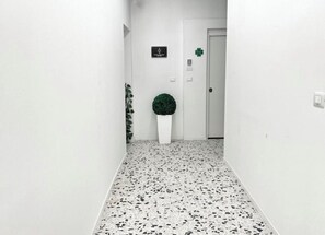 A hallway with a white wall, a door, a small plant, and a sign.