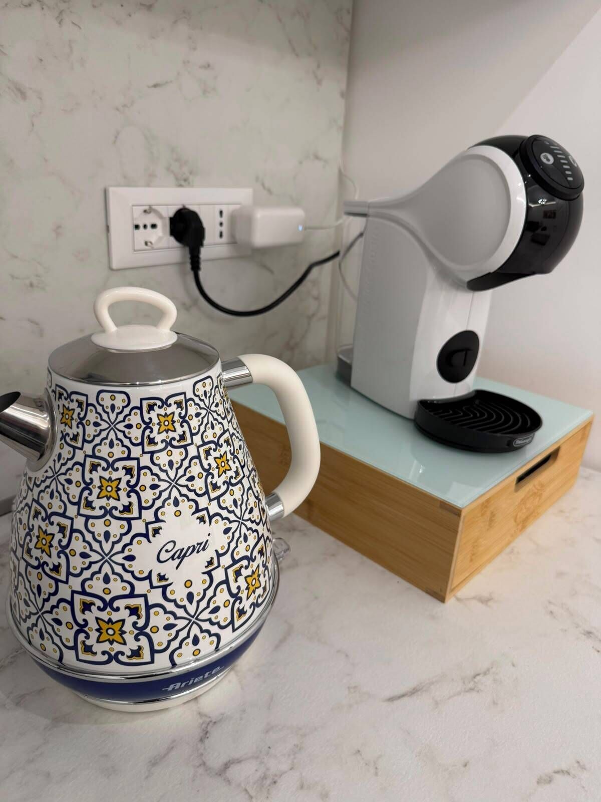 A kitchen with a patterned teapot, a hairdryer on a wooden box, and a power outlet.