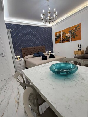 A modern bedroom with a tufted headboard, a dining table with a blue glass bowl, and a chandelier. - LUMìA Vatican Suite – Modernity and Comfort in the Heart of Rome (Roma)