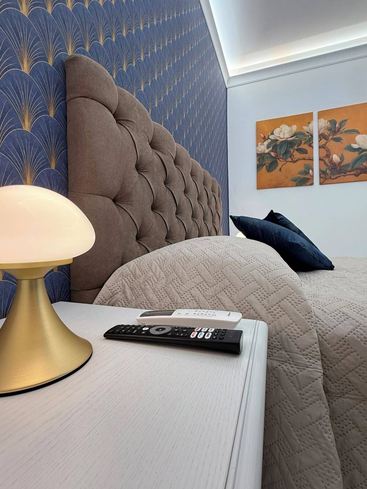 Une chambre d’hôtel avec une tête de lit capitonnée, une table de chevet avec une lampe, une télécommande et une couvre-lit matelassée.