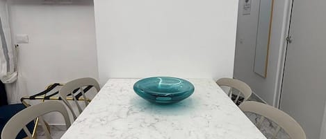 Un coin repas avec une table en marbre blanc, un bol turquoise et une horloge murale.