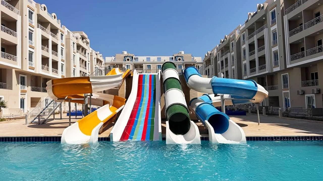 A swimming pool with multiple slides and a building with balconies in the background.