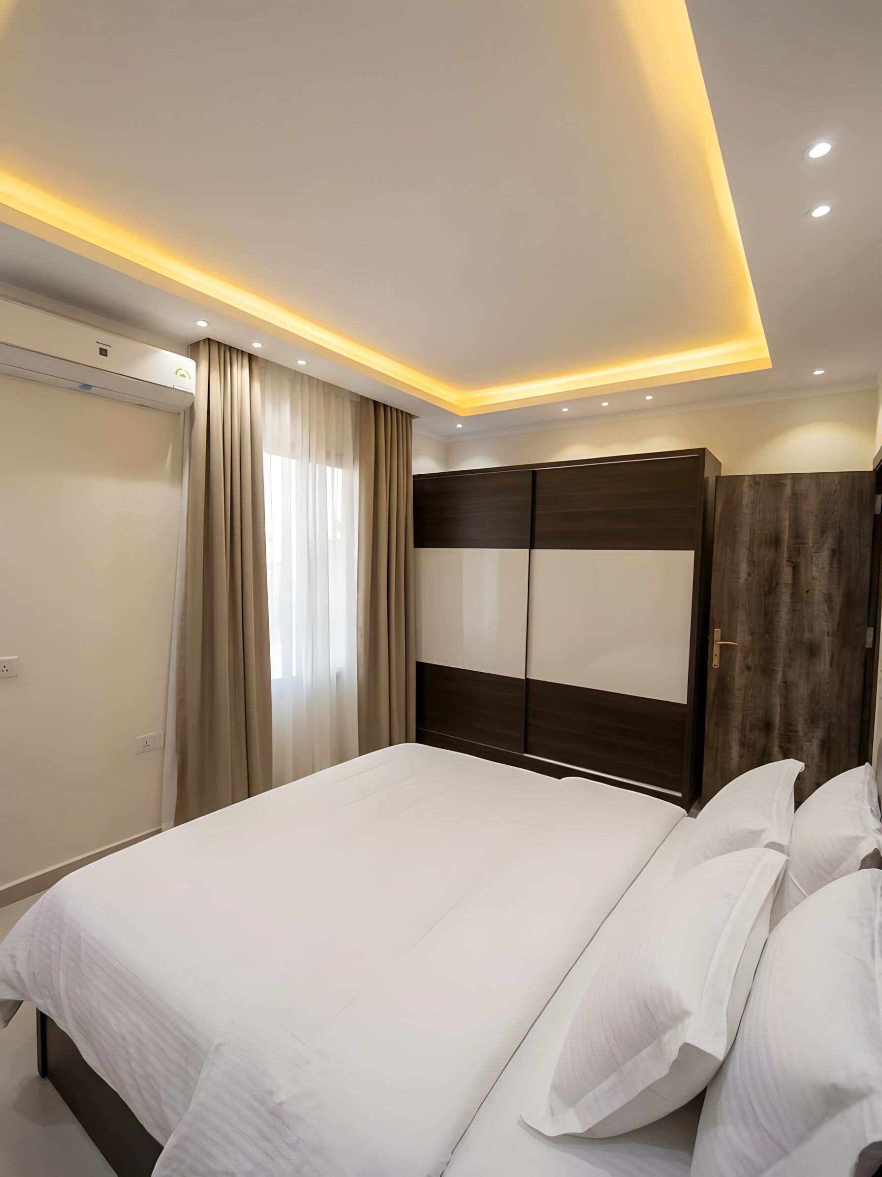 Moderni hotellihuone, jossa on suuri sänky, puinen vaatekaappi ja kattoon upotetut valaisimet.