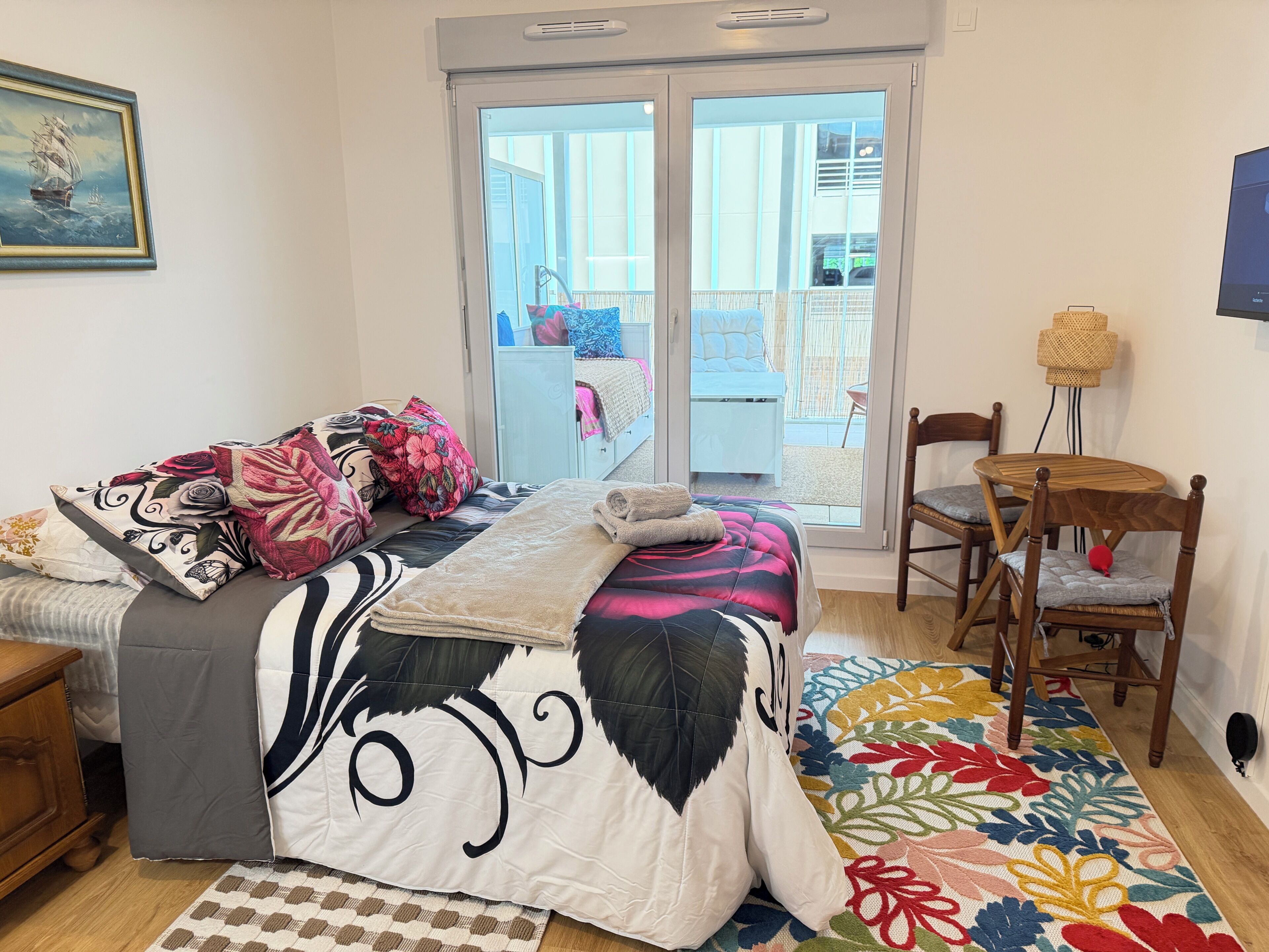 Une chambre à coucher avec un lit, une chaise, une petite table et une vue sur l’extérieur, visible à travers une porte vitrée.