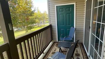 A covered porch with a view of a green door, a small table, and two chairs.