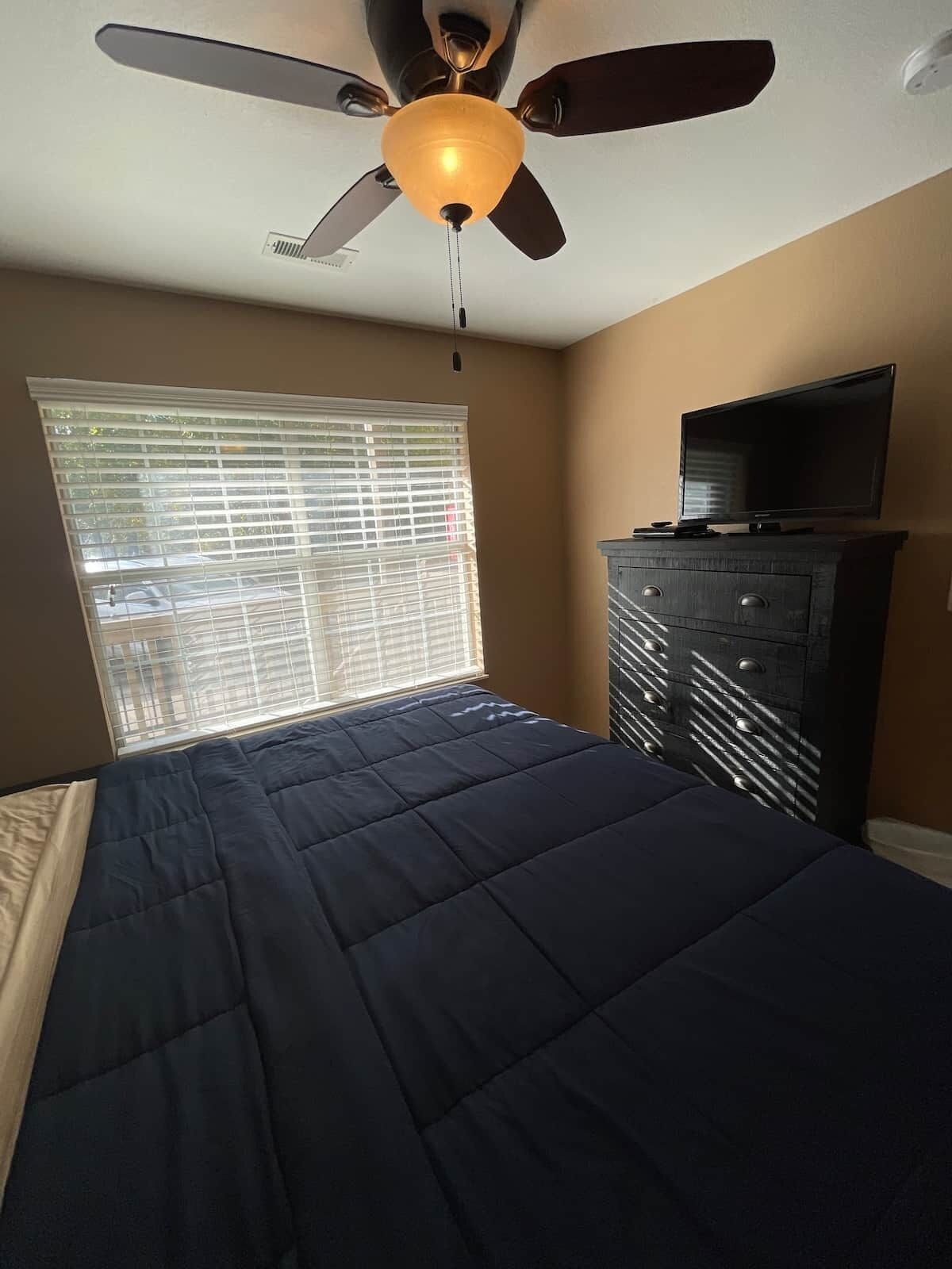 A bedroom with a bed, a ceiling fan, a dresser, and a television.