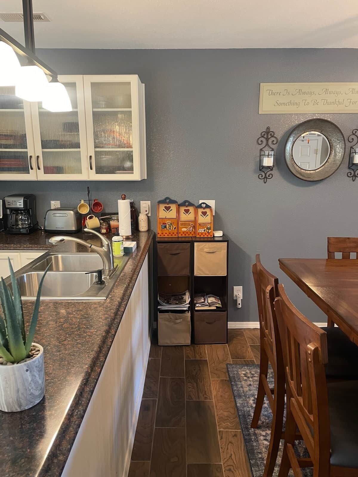 A kitchen with a built-in oven, a coffee maker, and a toaster. There is a dining table with chairs and a rug.