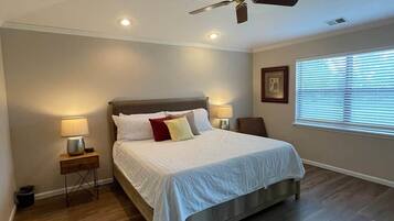Une chambre à coucher avec un lit, des tables de chevet, un ventilateur de plafond et une fenêtre avec des stores.