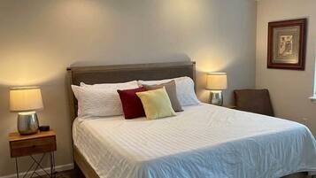 Une chambre à coucher avec un lit, deux tables de chevet avec des lampes, un ventilateur de plafond et un tableau encadré au mur.