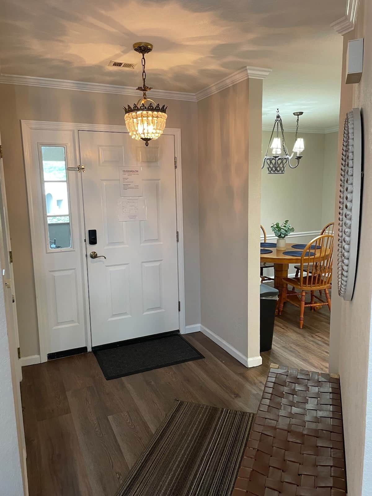 A hallway with a double door, a chandelier, a dining area with a table and chairs, and a patterned rug on the floor.