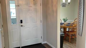A hallway with a double door, a chandelier, a dining area with a table and chairs, and a patterned rug on the floor.