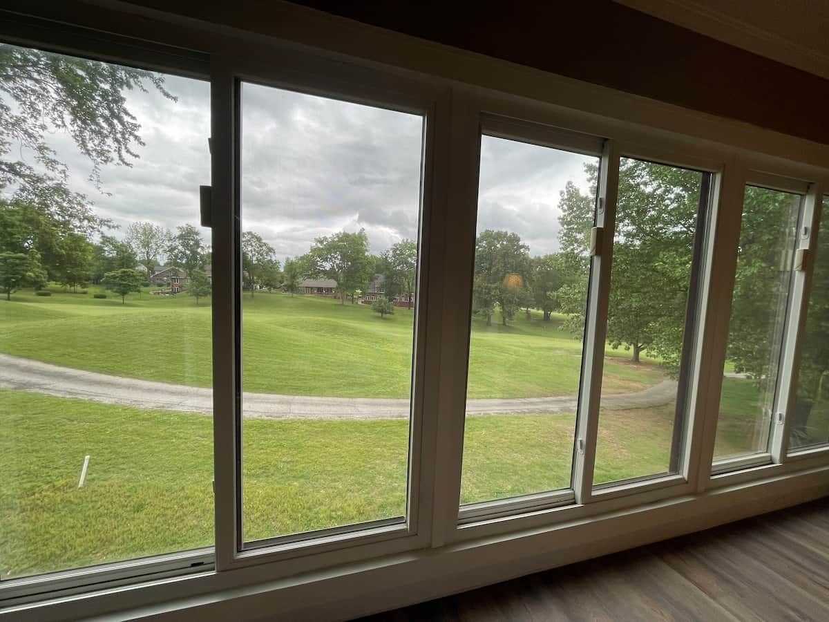 Ein Zimmer mit großen Fenstern und Blick auf eine Wiese und Bäume.
