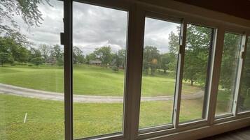 Ein Zimmer mit großen Fenstern und Blick auf eine Wiese und Bäume.