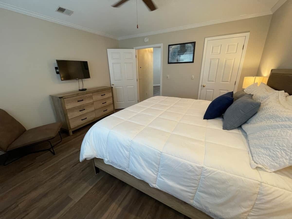 A bedroom with a large bed, a TV, a dresser, and a chair.
