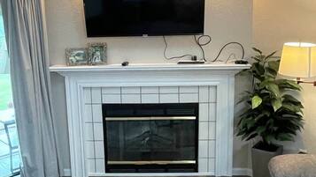 A living room with a fireplace, a flat-screen TV mounted above it, a glass coffee table, and a sofa.