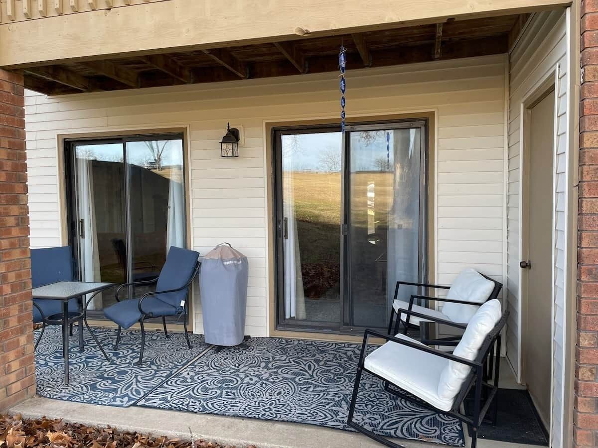 A covered patio with a table and chairs, a trash can, and a hanging light fixture.