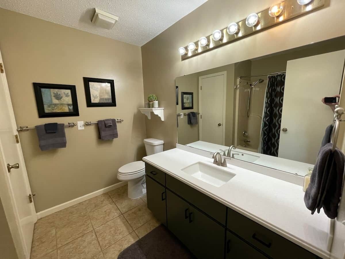 A bathroom with a white sink, a mirror, and a toilet. There are lights above the mirror and a towel rack with towels.