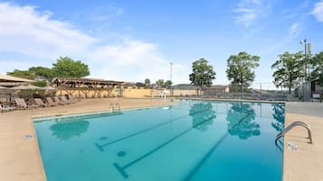 Une piscine à l’eau claire, entourée de chaises longues et de parasols, sous un ciel dégagé.