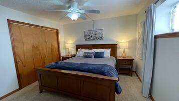 A bedroom with a wooden bed, a ceiling fan, two bedside tables with lamps, a door, and a window with curtains.
