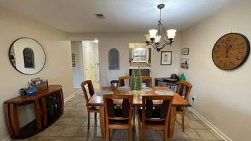 A dining area with a wooden table and chairs, a chandelier, a clock, and a sign that says 'let's eat.'