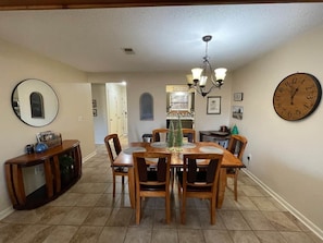 A dining area with a wooden table and chairs, a chandelier, a clock, and a sign that says 'let's eat.' - Pointe Royale Ground Level Walk-In With Golf View (Branson)