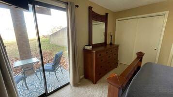 A bedroom with a bed, a dresser, a mirror, and a sliding glass door leading to an outdoor patio with a table and chairs.