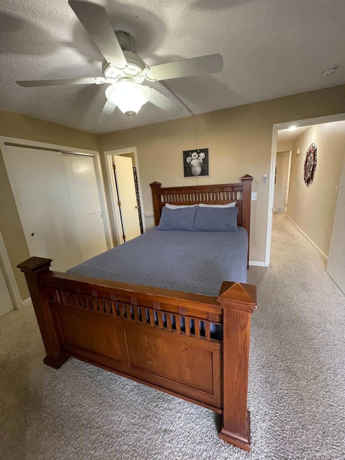 A bedroom with a wooden bed, a ceiling fan, and a carpeted floor.