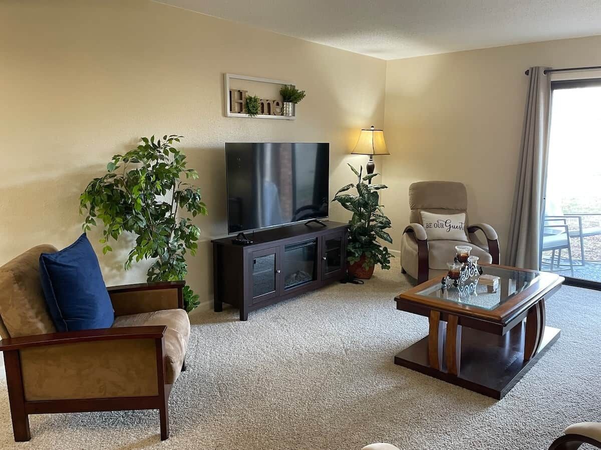 A living room with a sofa, a television, a coffee table, and two potted plants.