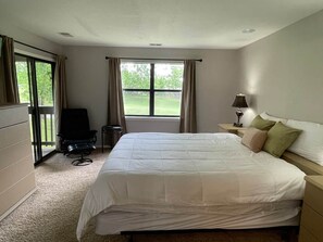 A bedroom with a bed, a chair, a nightstand, and a window. - Golf Front 4 Bedroom (Branson)