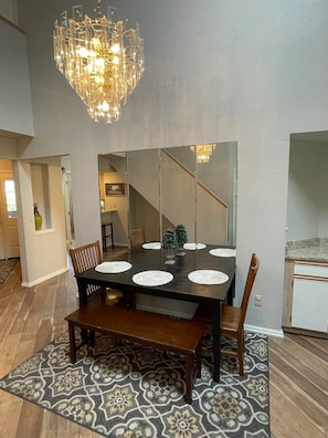 A dining area with a large table, chairs, a bench, a patterned rug, a chandelier, and a view of a staircase. - Golf Front 4 Bedroom (Branson)