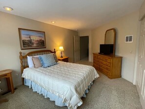 Une chambre à coucher avec un lit, une commode, un téléviseur, une lampe et un tableau accroché au mur.