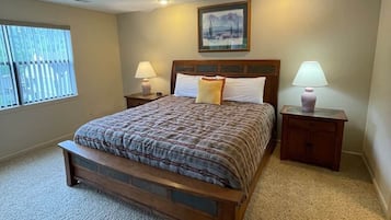 A bedroom with a large bed, two bedside tables with lamps, a window with blinds, and a painting on the wall.