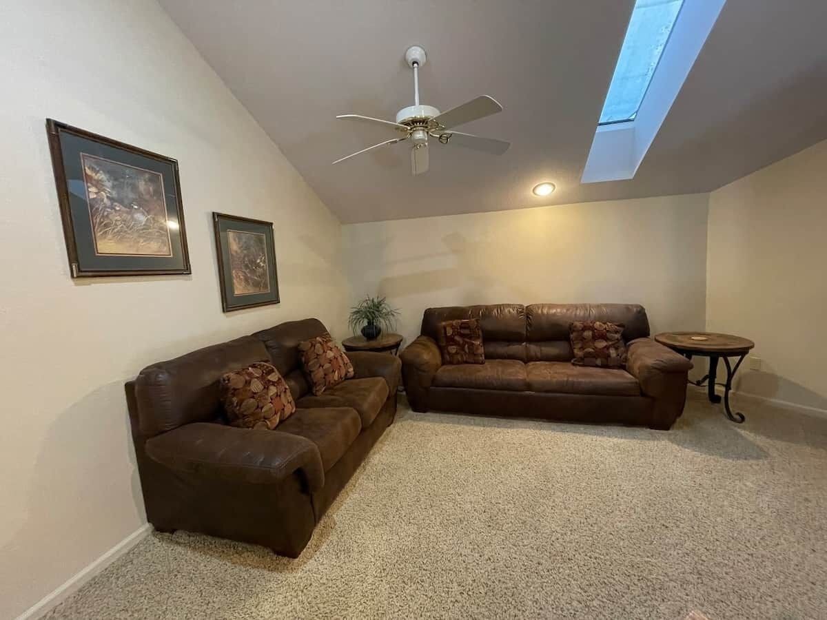 Ein Wohnzimmer mit zwei braunen Ledersofas, einem Deckenventilator, einem Oberlicht und gerahmten Kunstwerken an der Wand.