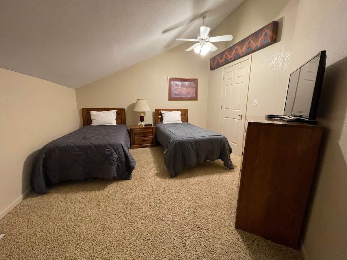 Une chambre avec deux lits, un ventilateur de plafond, une télévision et une porte.