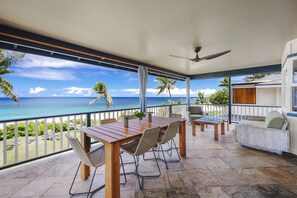 A covered outdoor area with a wooden table and chairs, a ceiling fan, and a view of the ocean. - Hale Pua Male at Ke Iki Beach (Haleiwa)