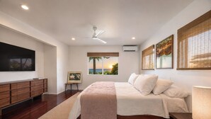 Quarto com cama, mesa de cabeceira e televisão sobre um suporte.