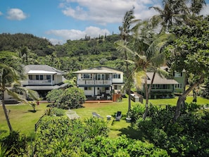 A two-story house with a balcony, surrounded by lush greenery and a well-maintained lawn. - Hale Pua Male at Ke Iki Beach (Haleiwa)