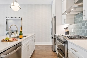 A modern kitchen with a stainless steel refrigerator, a gas stove, and a wine bottle on the counter. - 3 Homes Side by Side Rooftop Deck Sleeps 36 (Nashville)