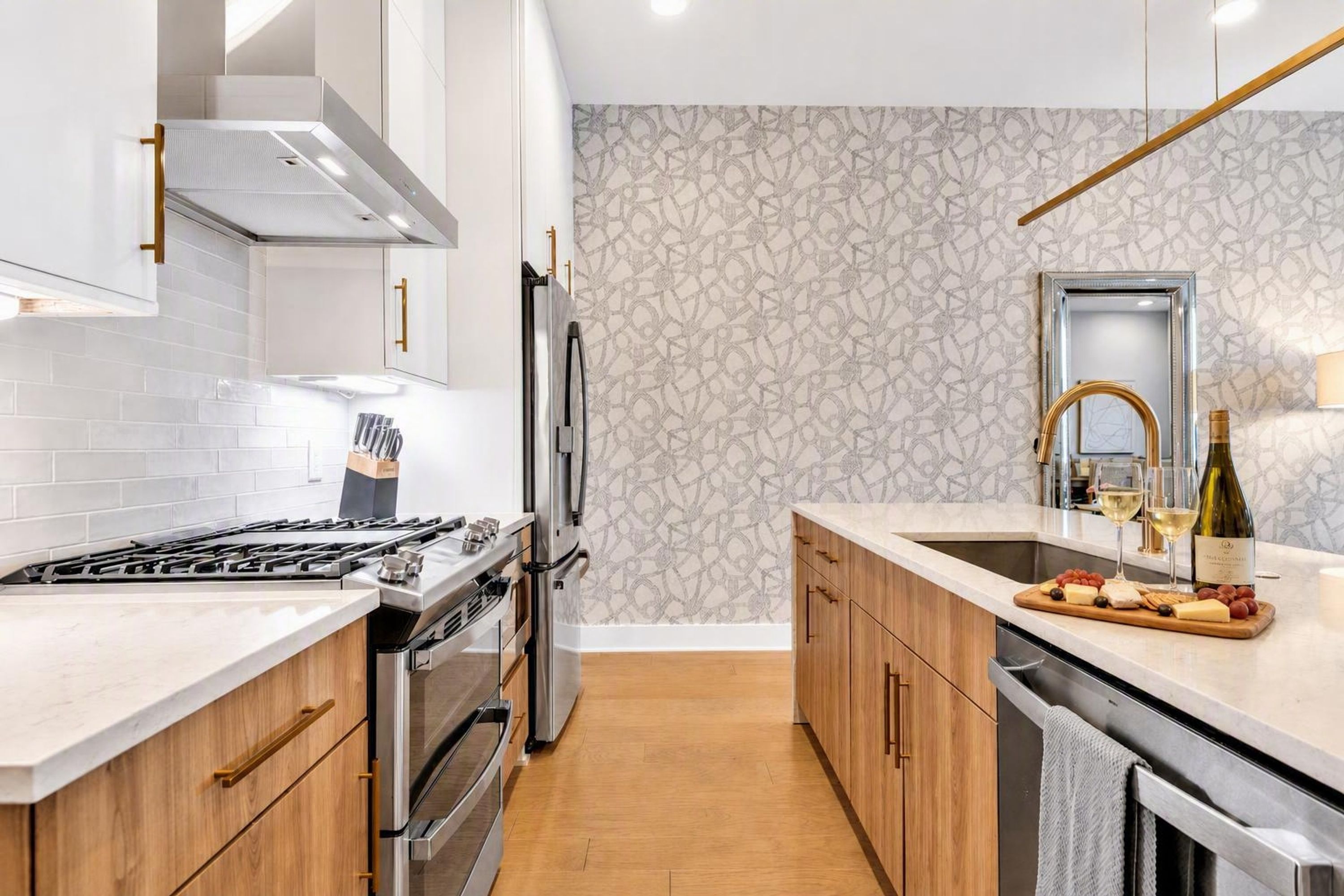 Een moderne keuken met een gasfornuis, roestvrijstalen apparatuur, houten kastjes en een marmeren spatwand.