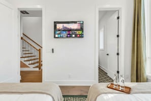 A hotel room with a TV mounted on the wall, a staircase, and a bed with a tray of glasses. - 3 Homes Side by Side Rooftop Deck Sleeps 36 (Nashville)