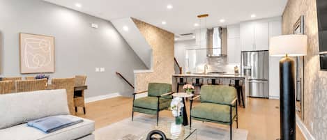 Ein modernes Wohnzimmer mit einer Couch, Sesseln, einem Couchtisch und einer Küche im Hintergrund.