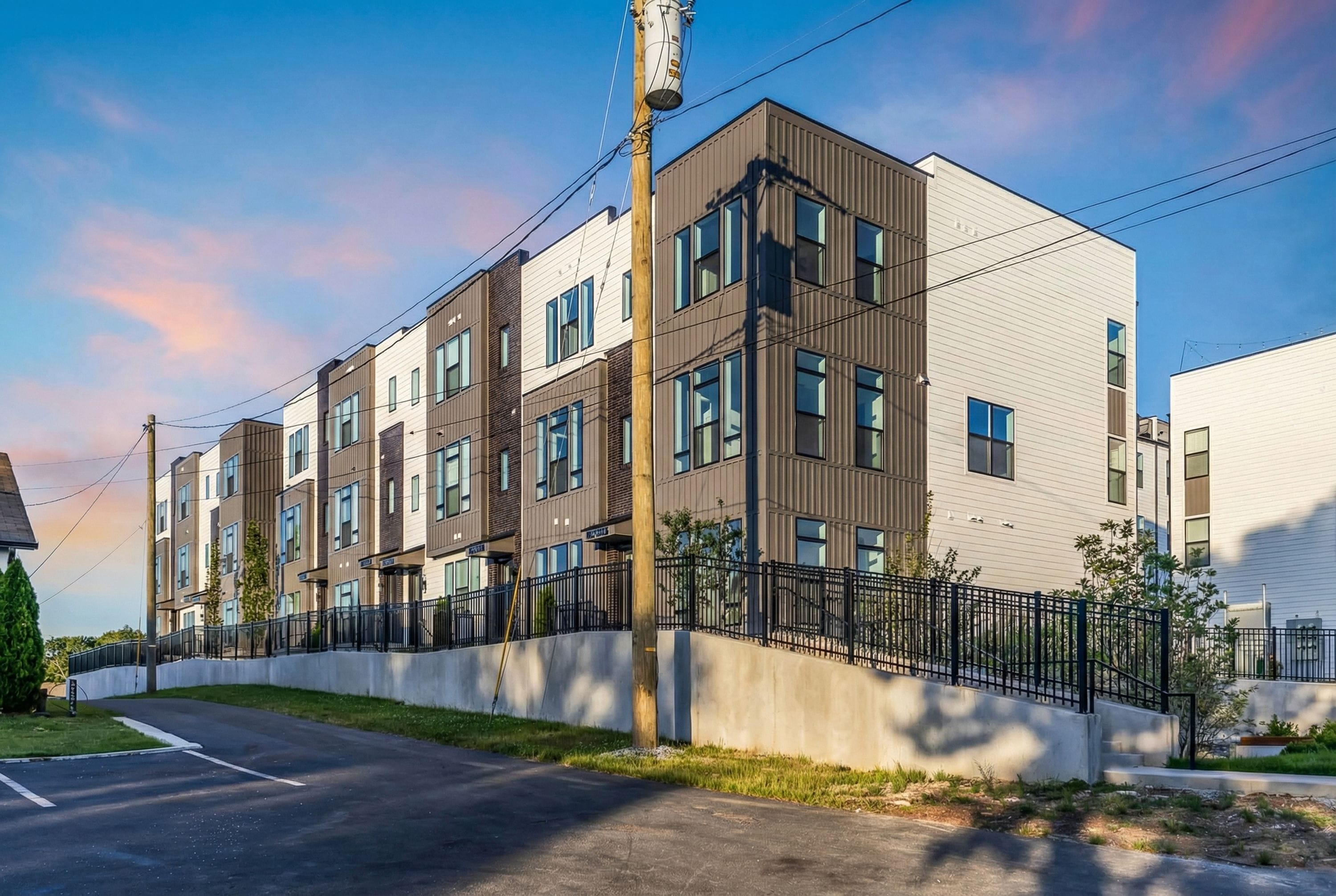 A multi-story residential building with a modern architectural design, featuring a mix of brick and siding exteriors, large windows, and a gated entrance.