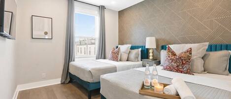 Habitación de hotel con dos camas, ventilador de techo, pared con diseño y ventana con cortinas.