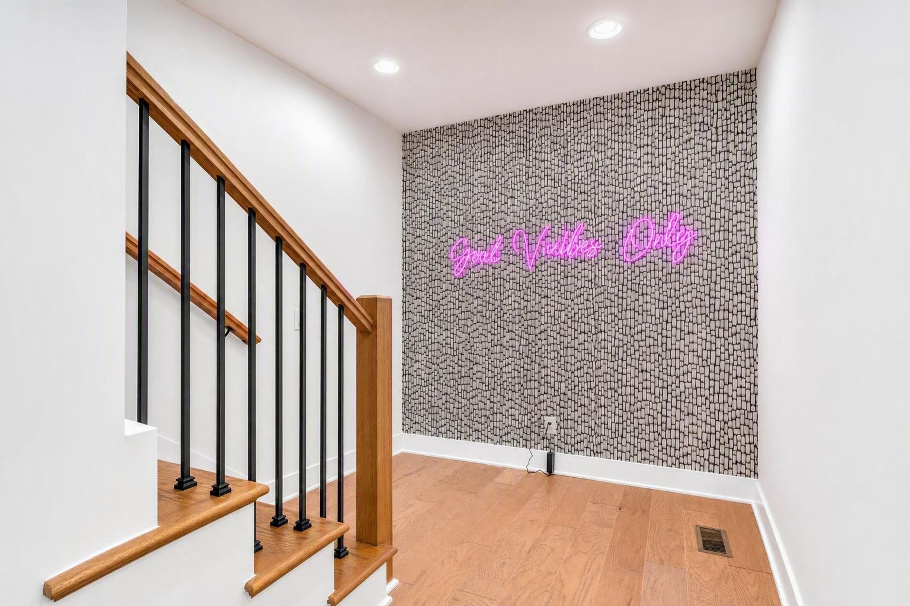 A staircase with wooden handrails and a patterned wall with a neon sign.