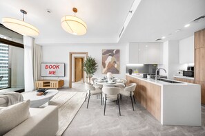 A modern kitchen with a central island, dining area with chairs, and a living space with a sofa and a coffee table. - Stayshort - 2 Bedroom in Business Bay Sleeps 6 With Water Canal Views (Dubai)